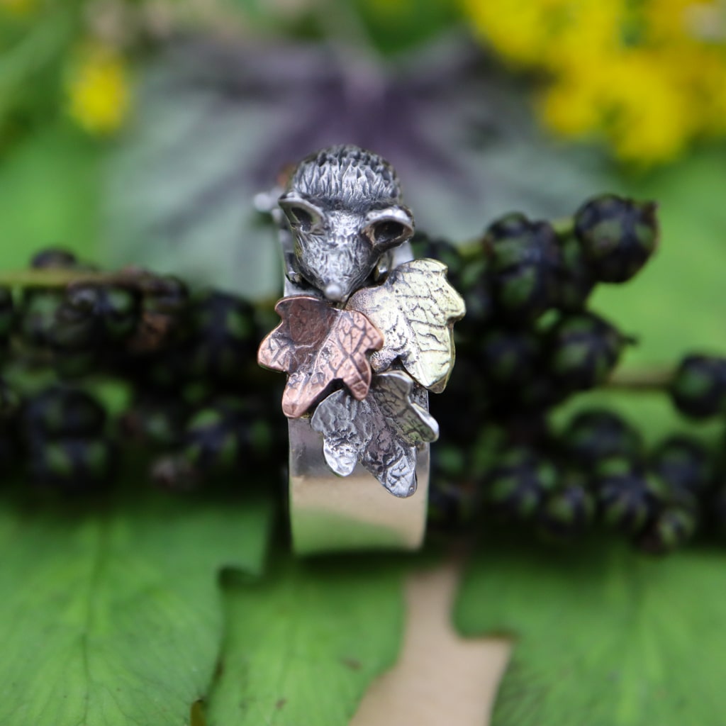 A sterling silver ring featuring a tiny hand carved mouse in the center of copper, brass, and silver fall leaves. this is a photo of the face and tiny nose of the fluffy mouse.