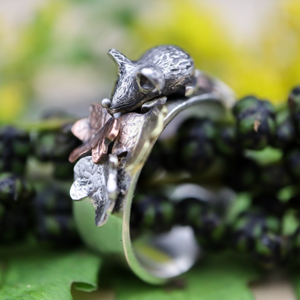 A sterling silver ring featuring a tiny hand carved mouse in the center of copper, brass, and silver fall leaves.
