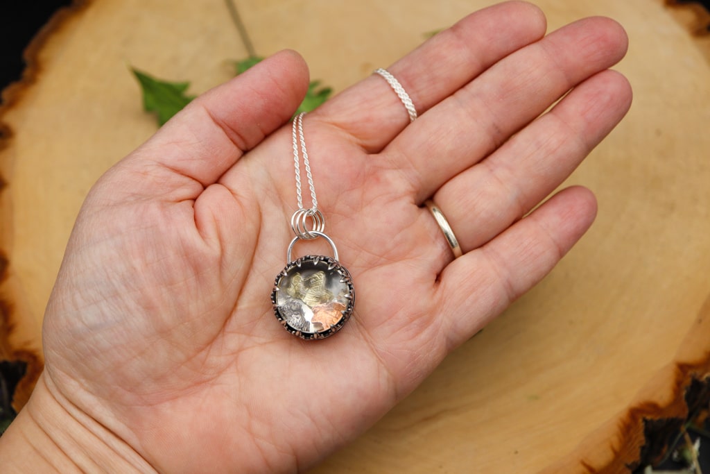 A hand is shown holding the foraging mouse necklace. The pendant is about 1.5 inches tall and made from sterling silver.