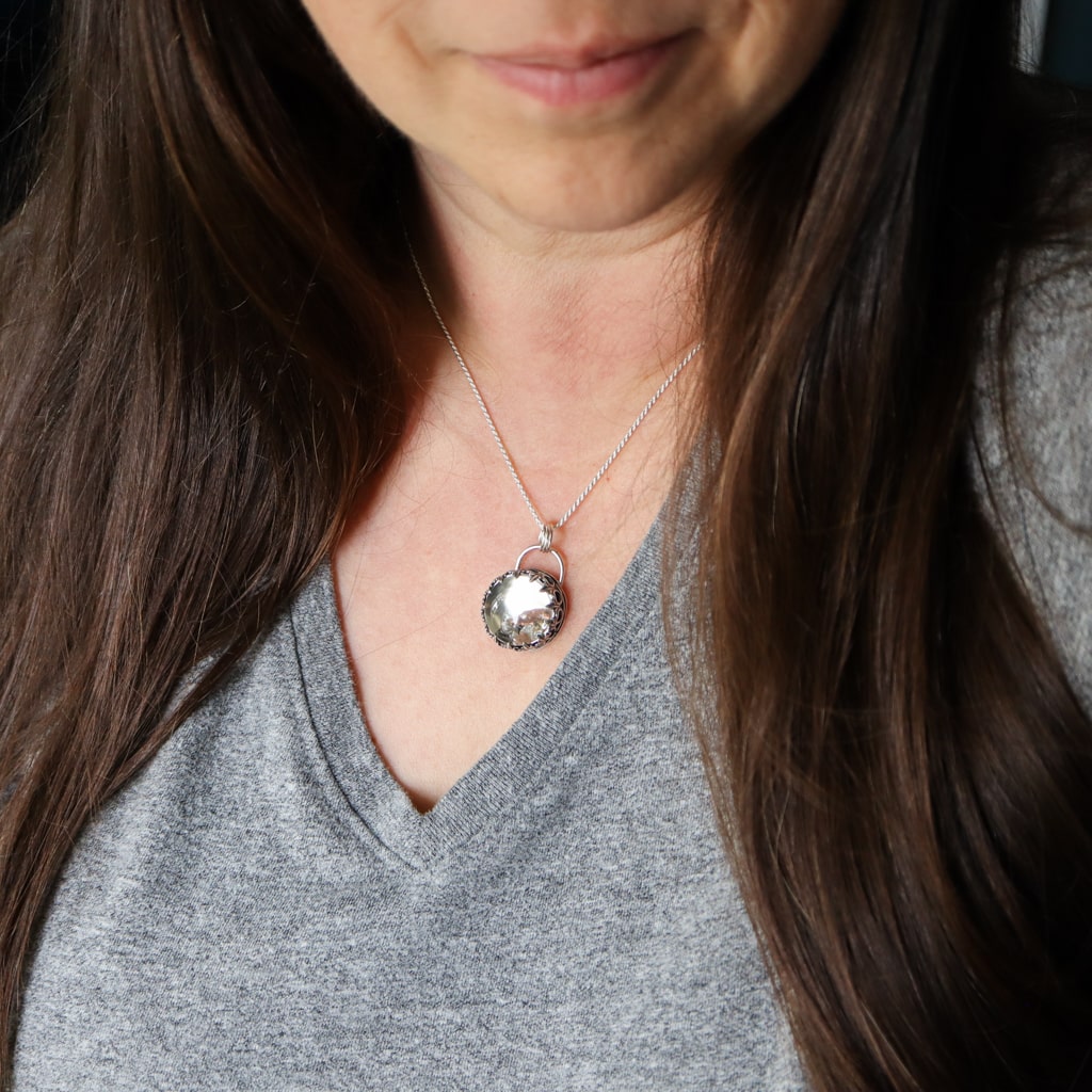 A woman with long hard hair is shown wearing the foraging mouse pendant. She is wearing a grey v neck shirt and slightly smiling.