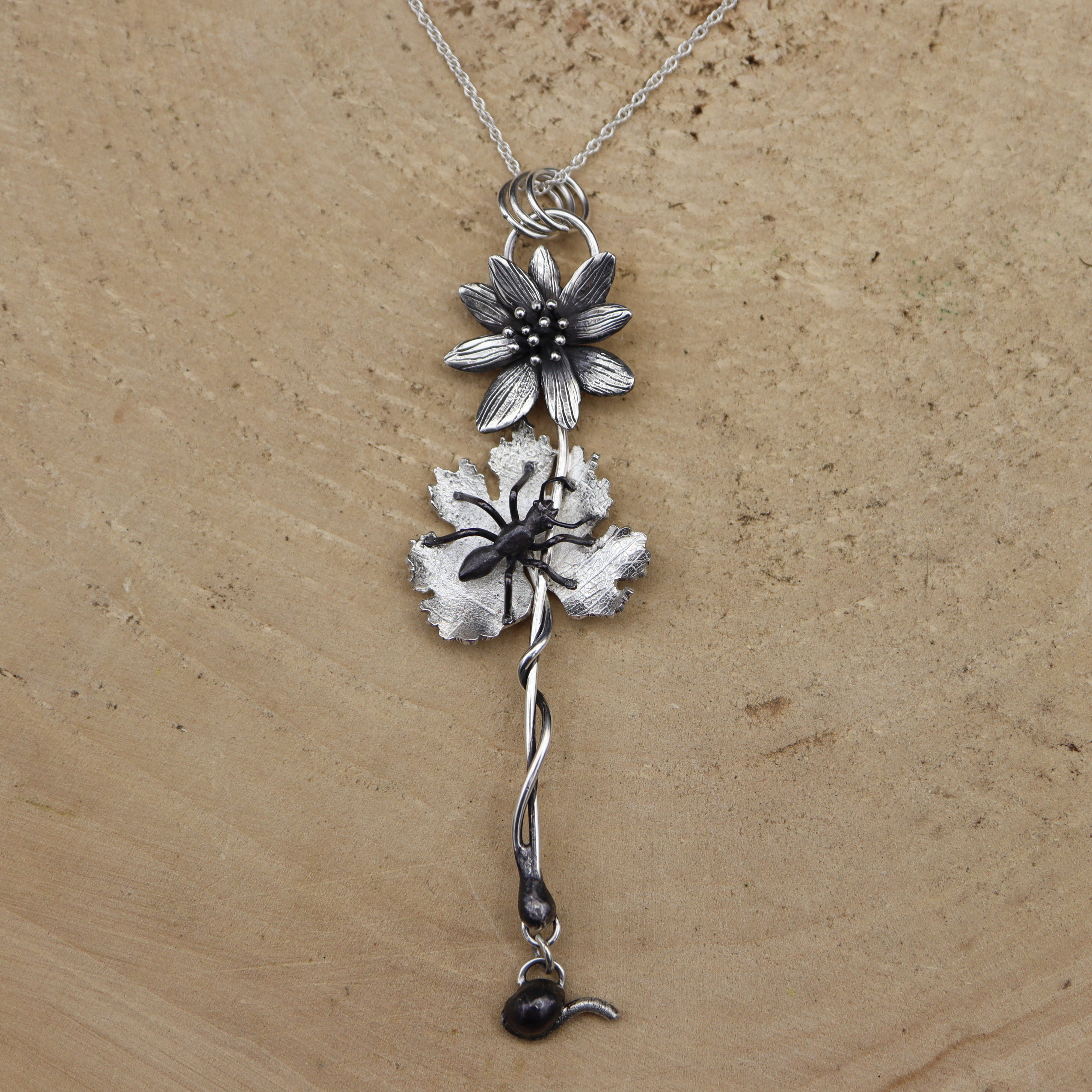 Silver native bloodroot flower necklace on a beige wood .background