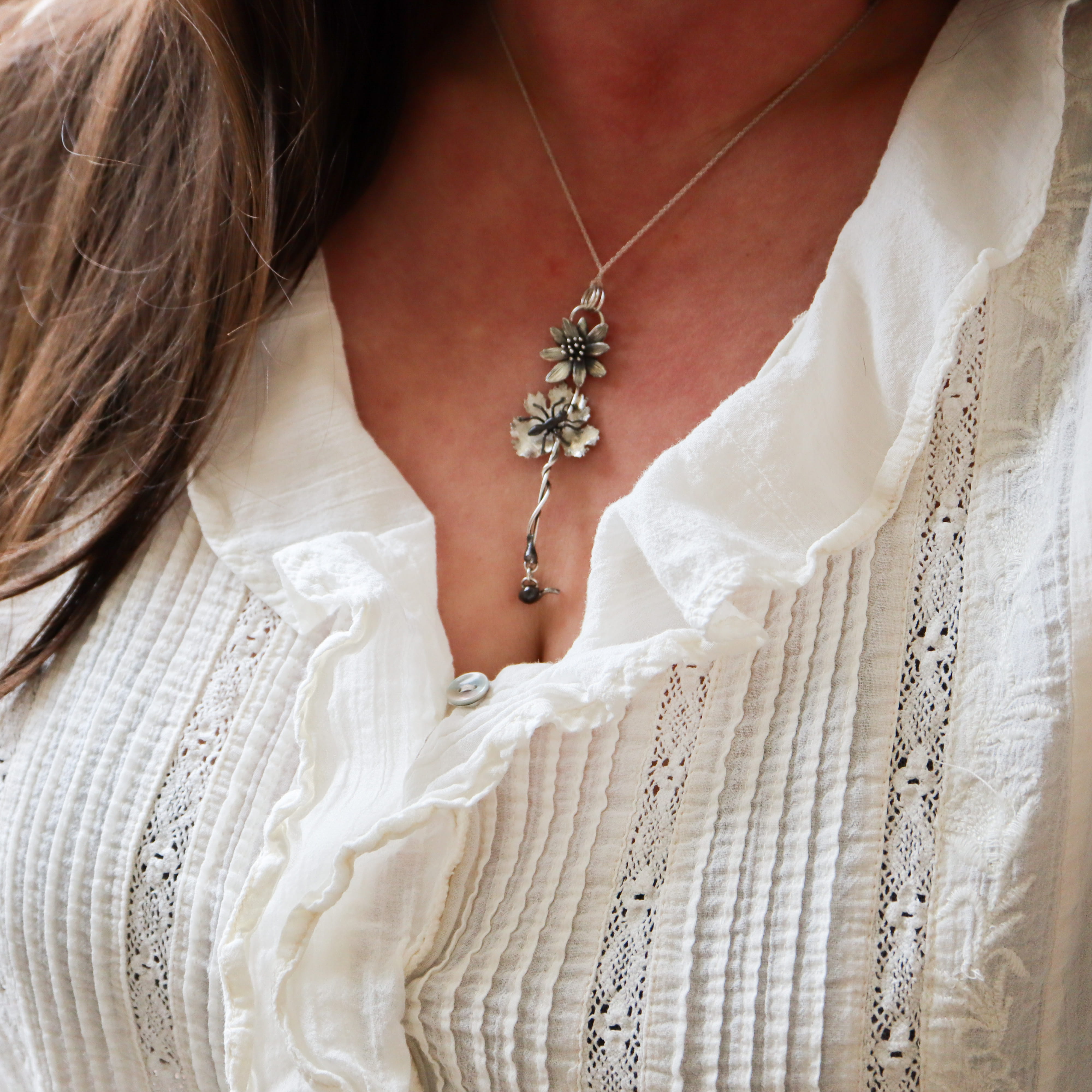 Close-up of a woman wearing a delicate sterling silver bloodroot flower necklace against a white blouse.