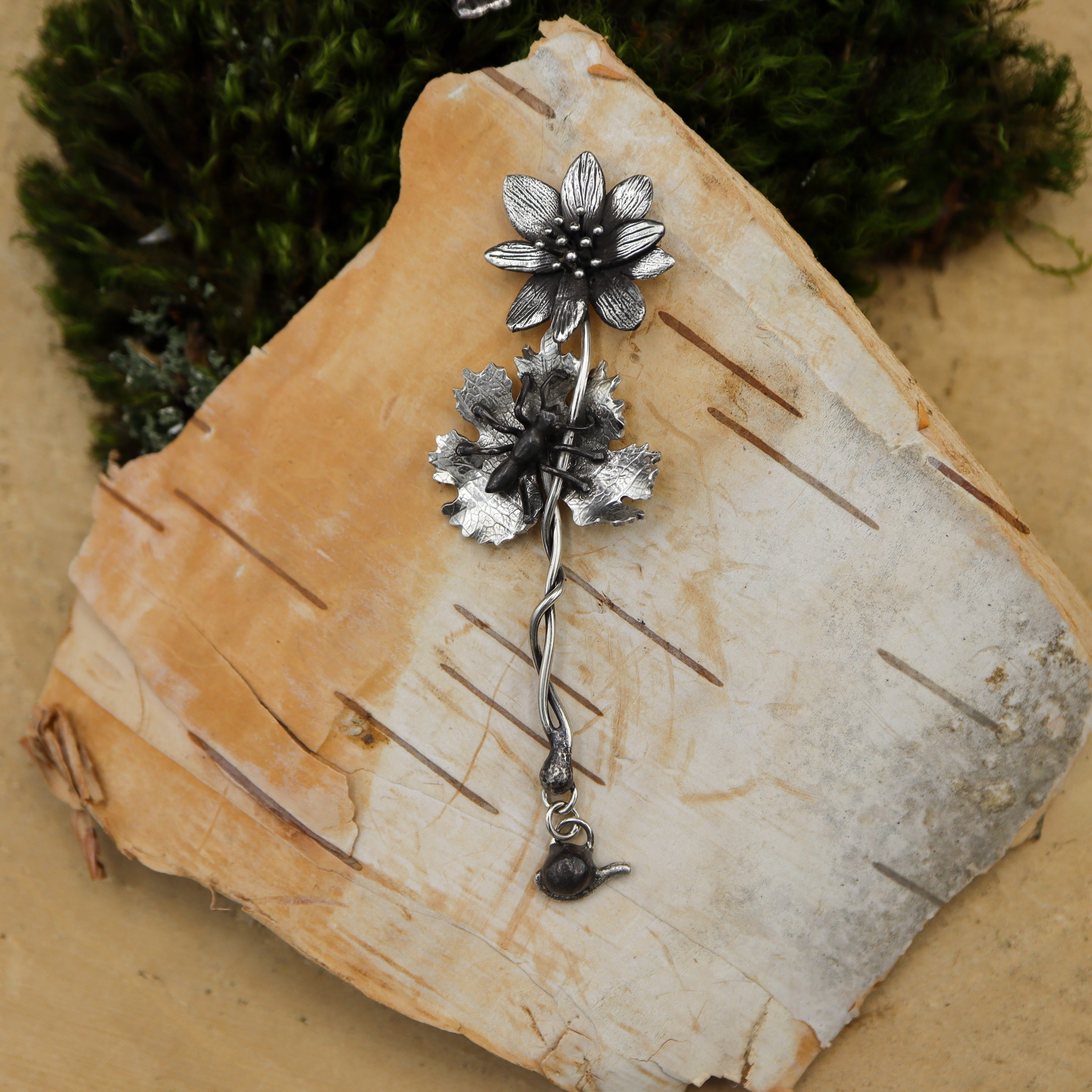 A handmade sterling silver bloodroot flower pin that also has a tiny ant on the leaf.