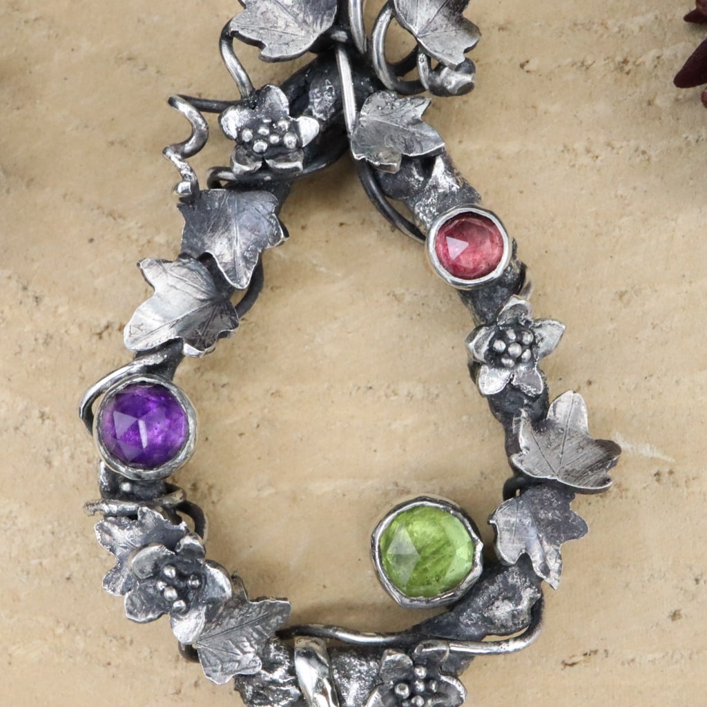 A close up of the three rose cut gemstones. A pink tourmaline, purple amethyst, and a green peridot gemstone.