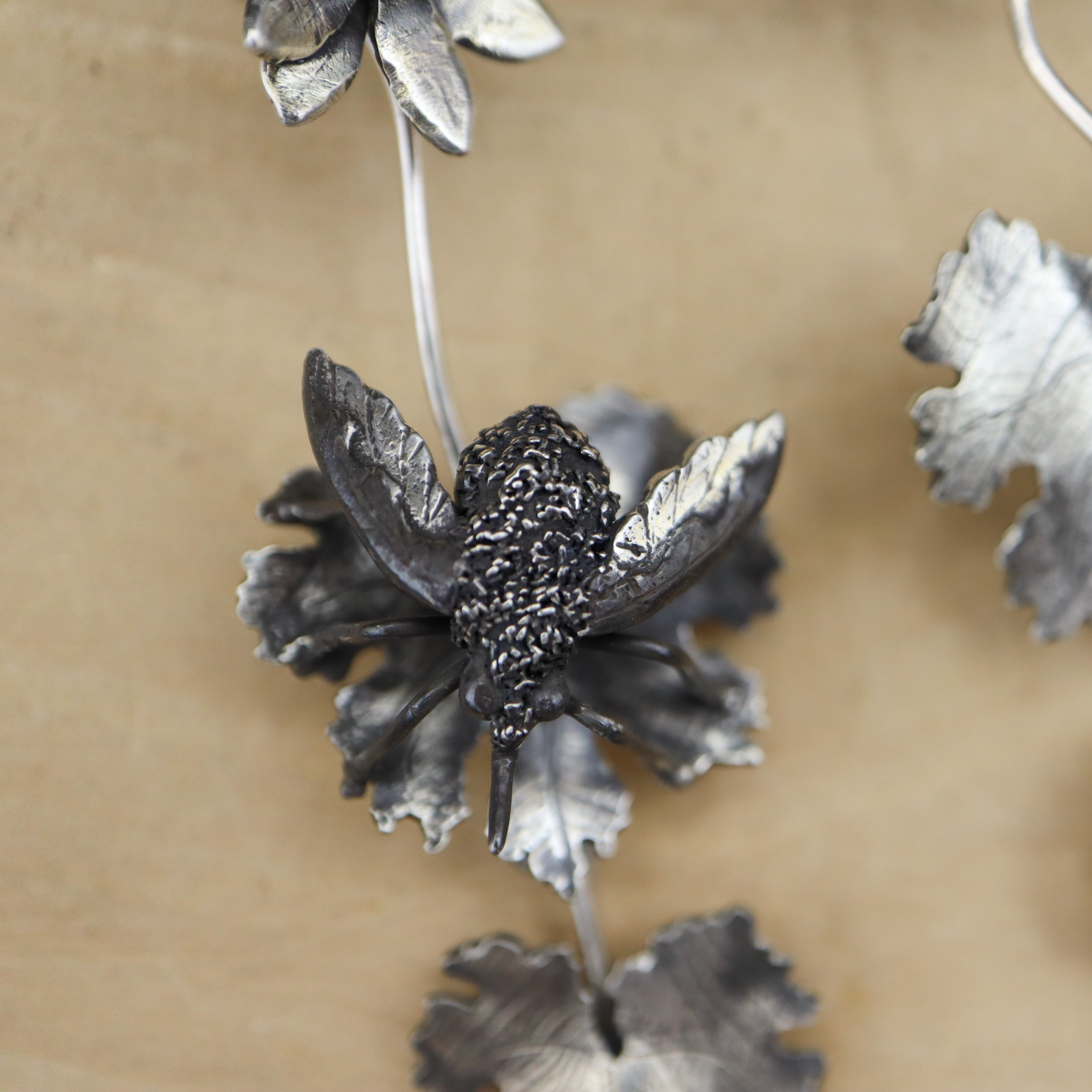 A close up photo of a sterling silver bee fly on a bloodroot flower on a pair of earrings.