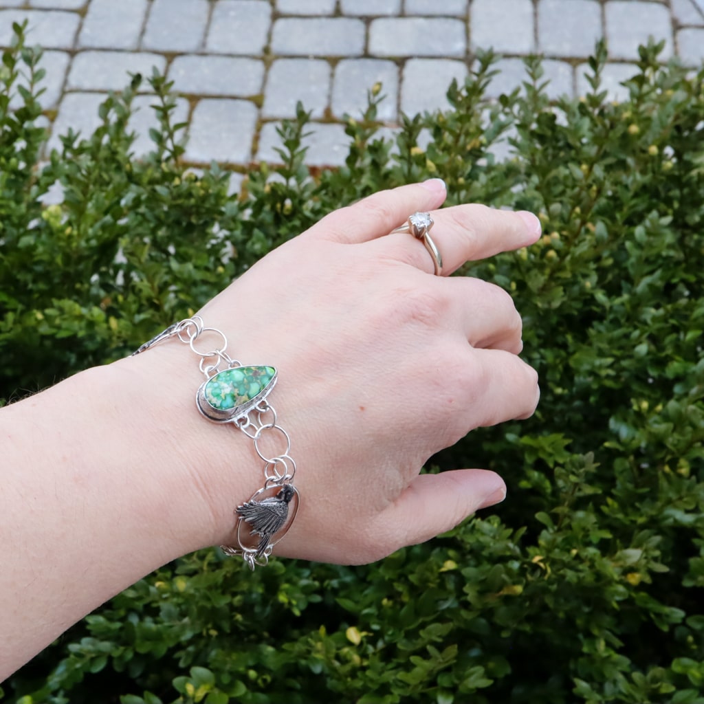 The chickadee bracelet is shown being worn outdoors with some bushes in the background.
