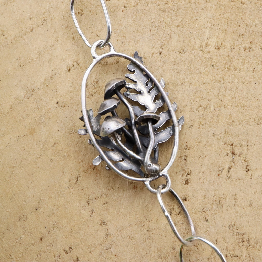 A close up of the necklace chain that has a reversible link featuring mushrooms and ferns.