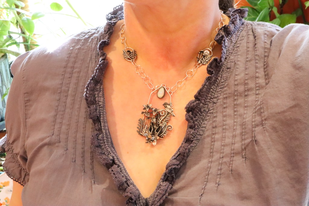 The necklace is shown being worn by a woman in a v cut purple shirt.