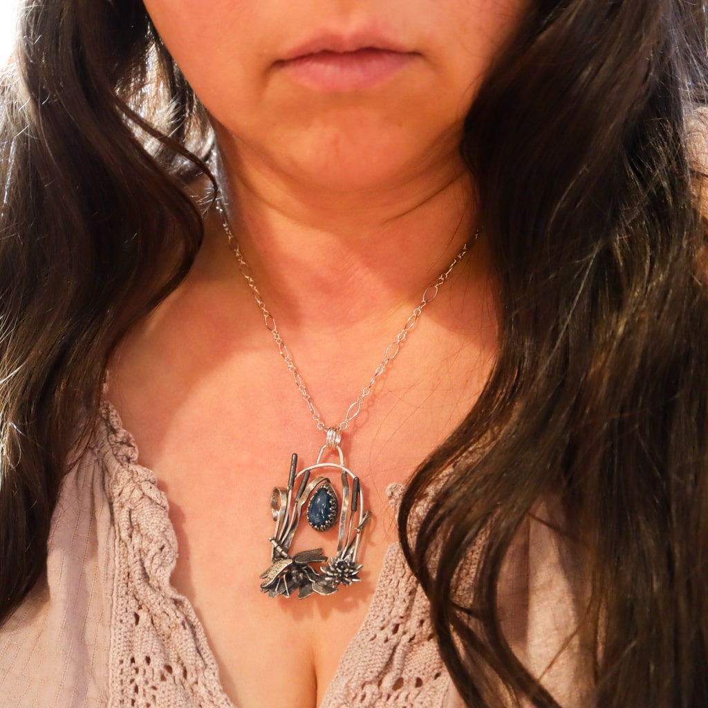 A woman with long dark brown hair is shown wearing the dragonfly necklace.