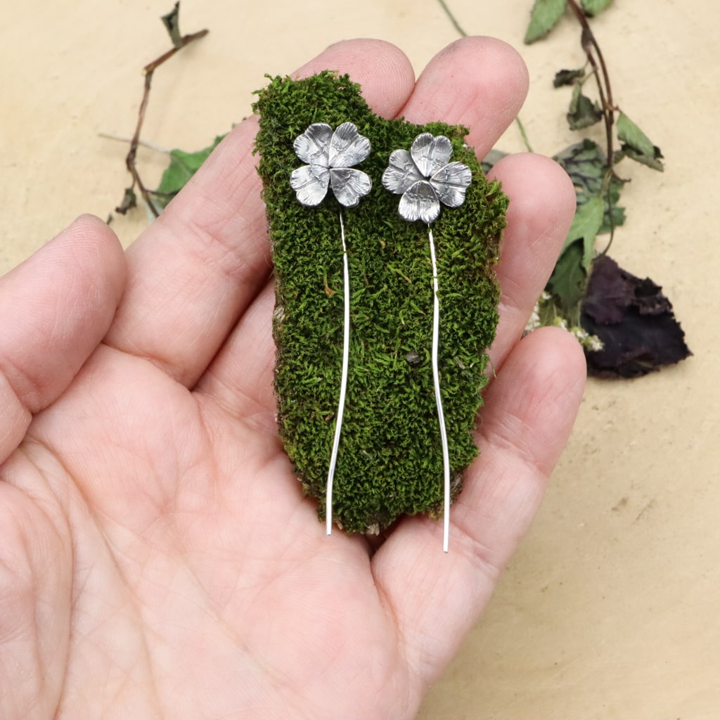 A hand is shown holding the sterling silver 4 leaf clover earrings for size reference. They are abut 2.5 inches long.