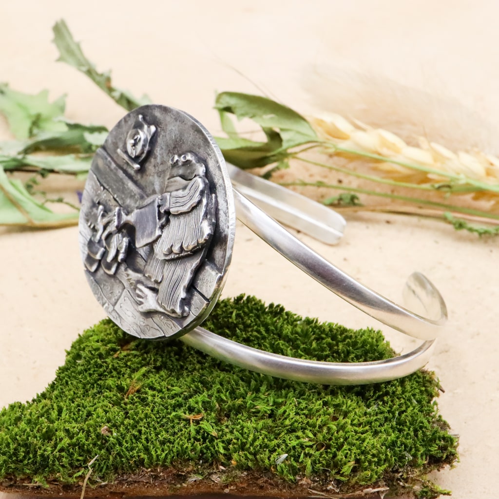 A side view of the sterling silver Frog & Toad bracelet. It is shown on a piece of dark green moss.