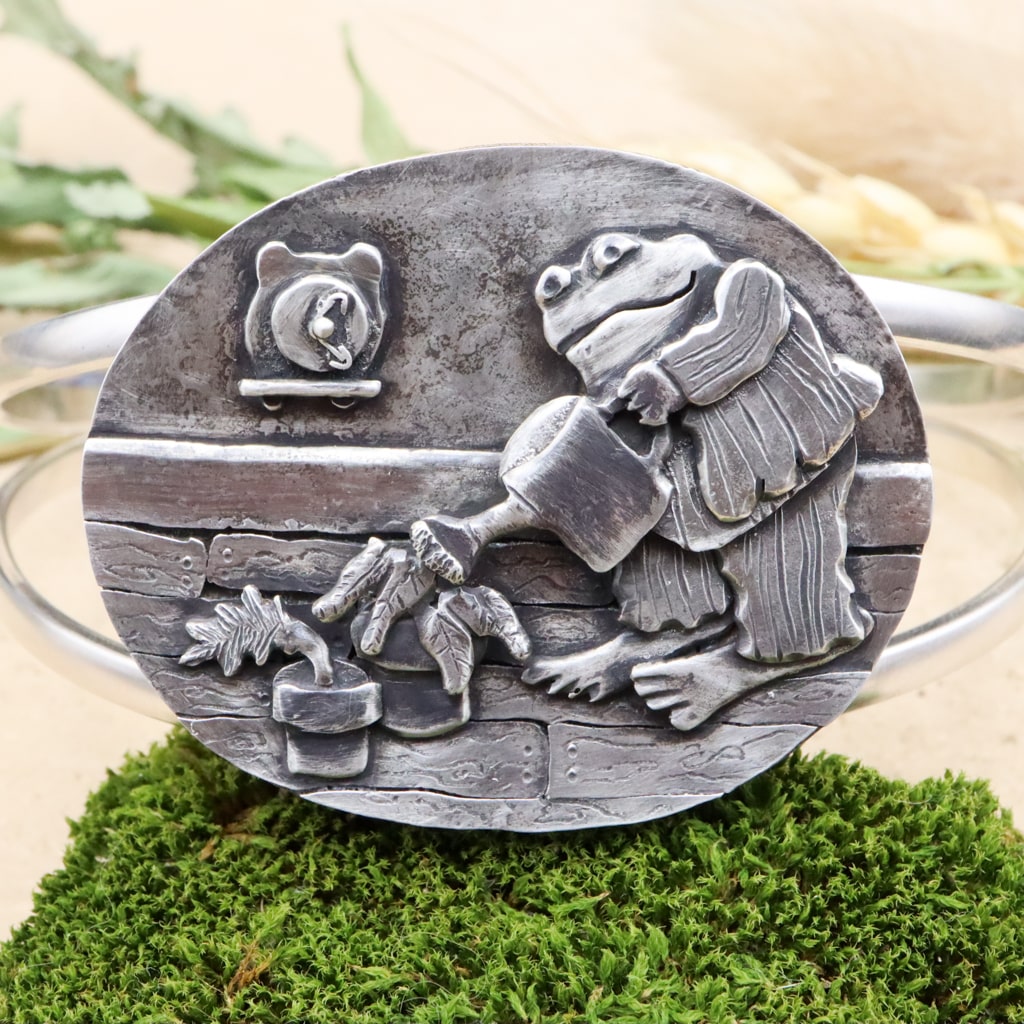 Toad from Frog & toad is shown watering his houseplants as a form of "self-care". This is a bracelet made from sterling silver and shown on a piece of dark green moss.