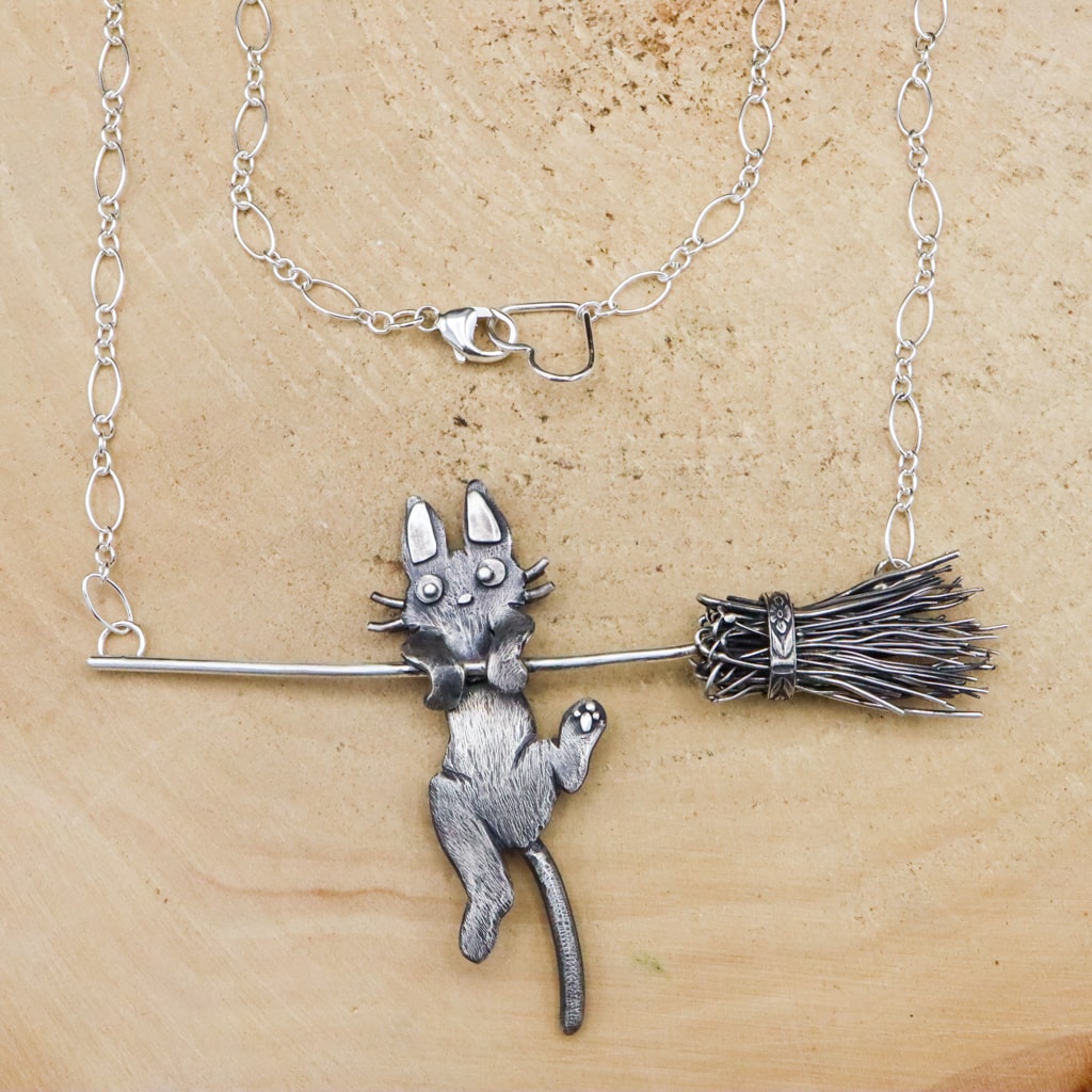 A sterling silver handmade Jiji necklace from Kiki's Delivery Service. He is shown hanging onto a broom handle and partially falling off.
