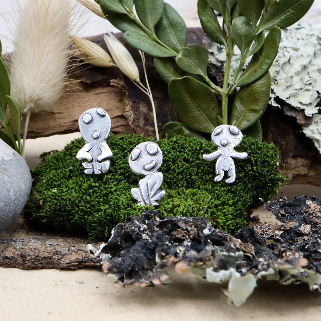 Sterling silver kodama earring studs are shown on a piece of dark green moss. They are each about 1/2 inch tall and handmade.