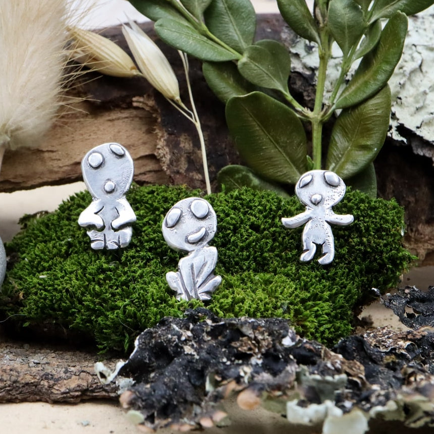 Sterling silver kodama earring studs are shown on a piece of dark green moss. They are each about 1/2 inch tall and handmade.