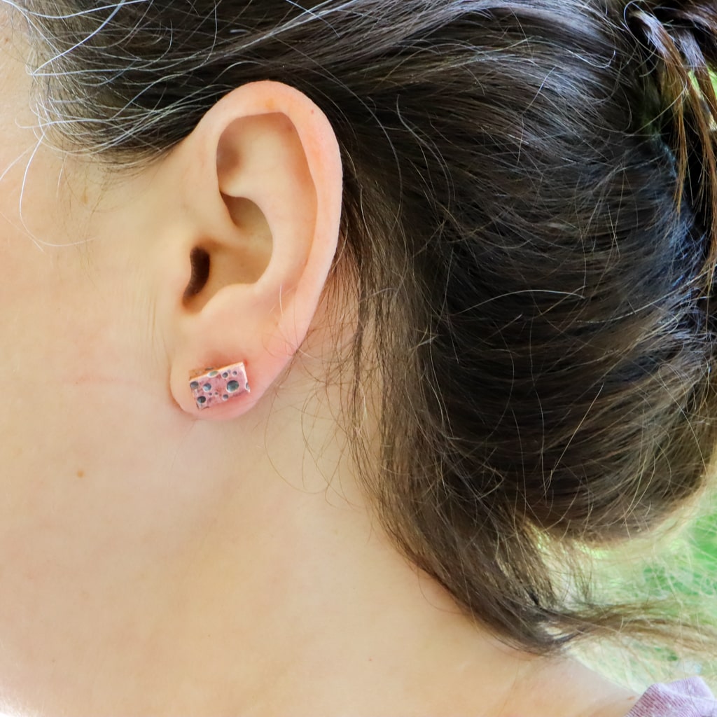 Someone shown wearing a tiny piece of copper swiss cheese as an earring. It is made from copper.