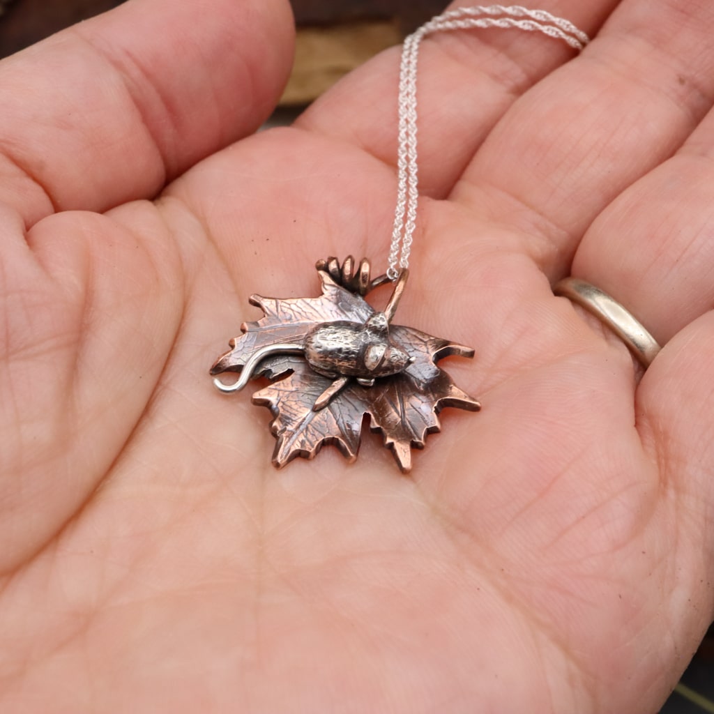 A side view of the maple leaf and mouse necklace shown in a hand.