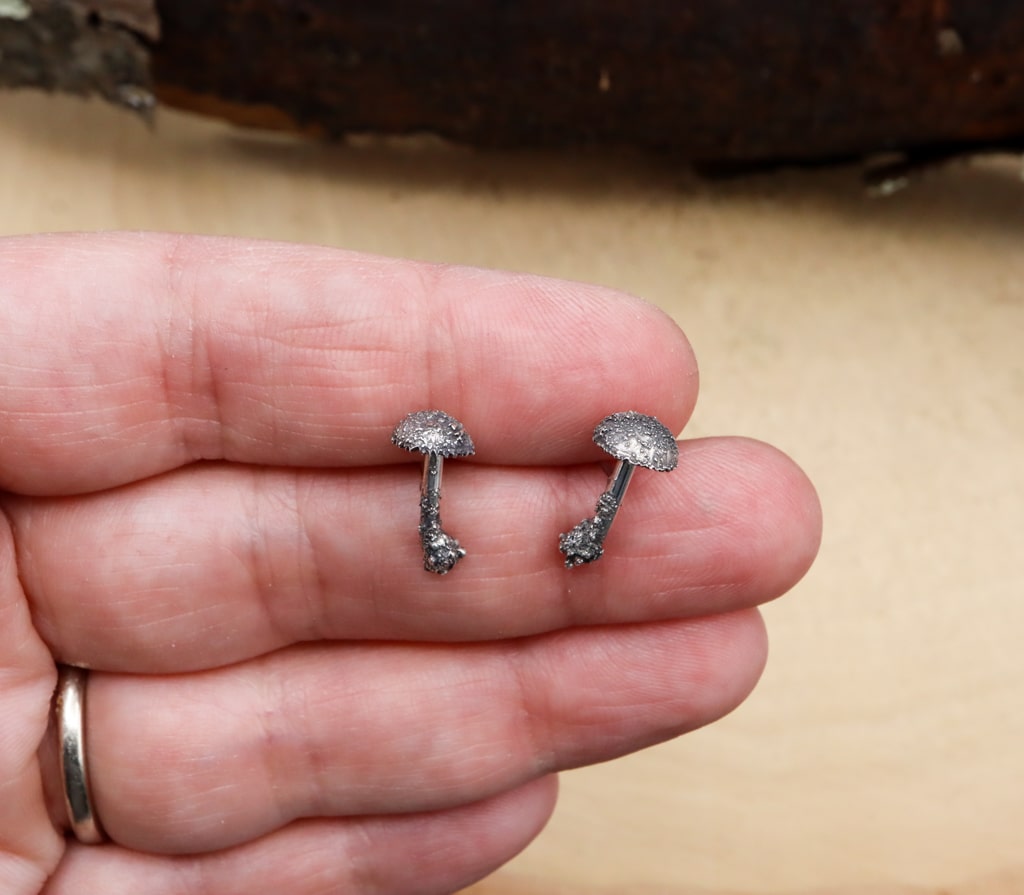 A hand is shown holding the 1/2 inch tall sterling silver mushroom stud earrings.
