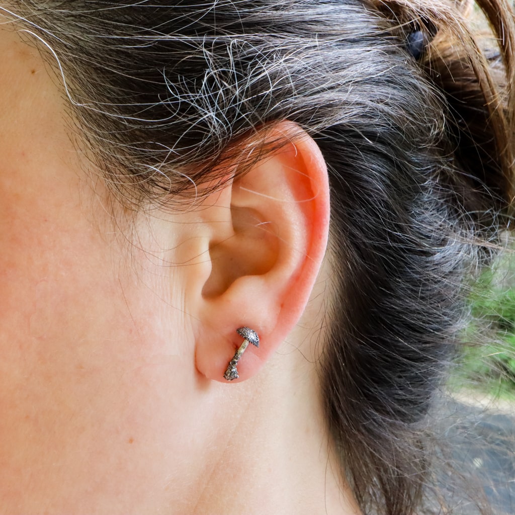 Sterling silver hand carved small mushroom stud earrings are shown being worn.