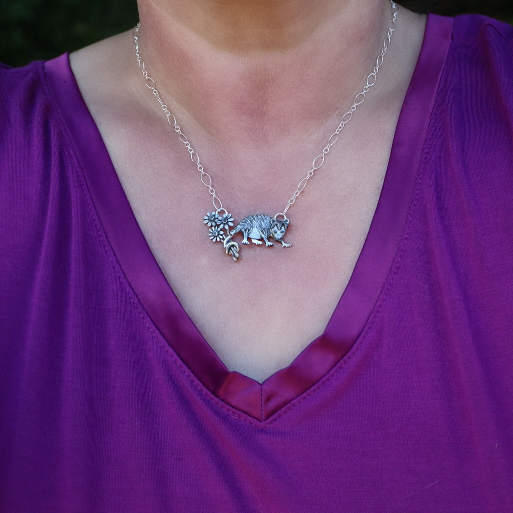 A close up of a woman wearing the sterling silver Virginia opossum necklace wearing a dark purple v-neck shirt.