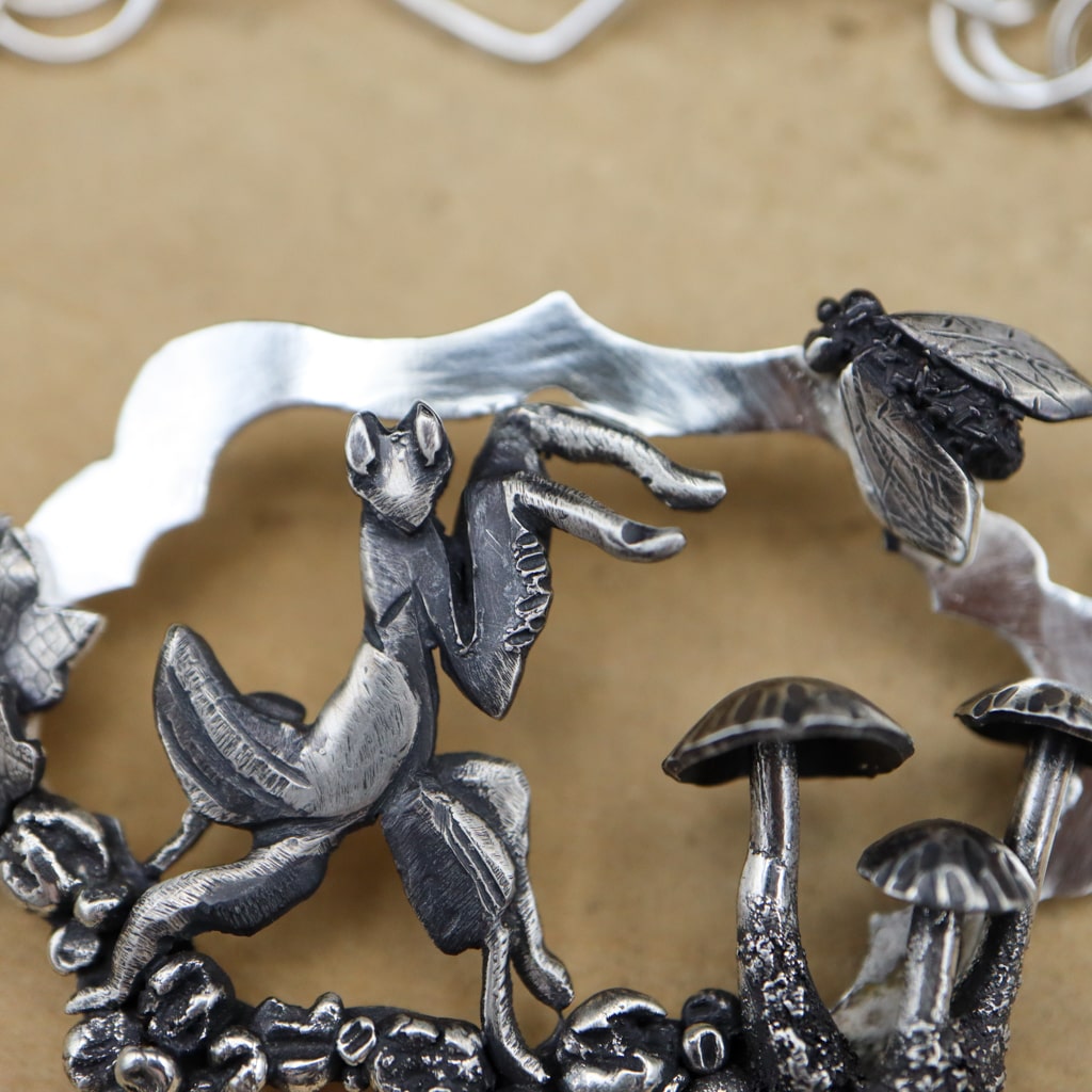 A close up photo of the orchid mantis bracelet showing the little mushrooms and silver fly.