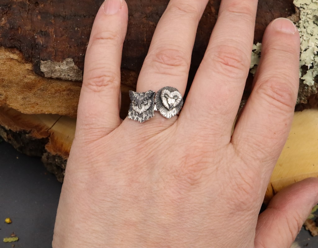 A hand is shown wearing two sterling silver owl face rings stacked on top of each other. These handmade owl rings are only about 1/2 inch tall and come in all sizes for women.