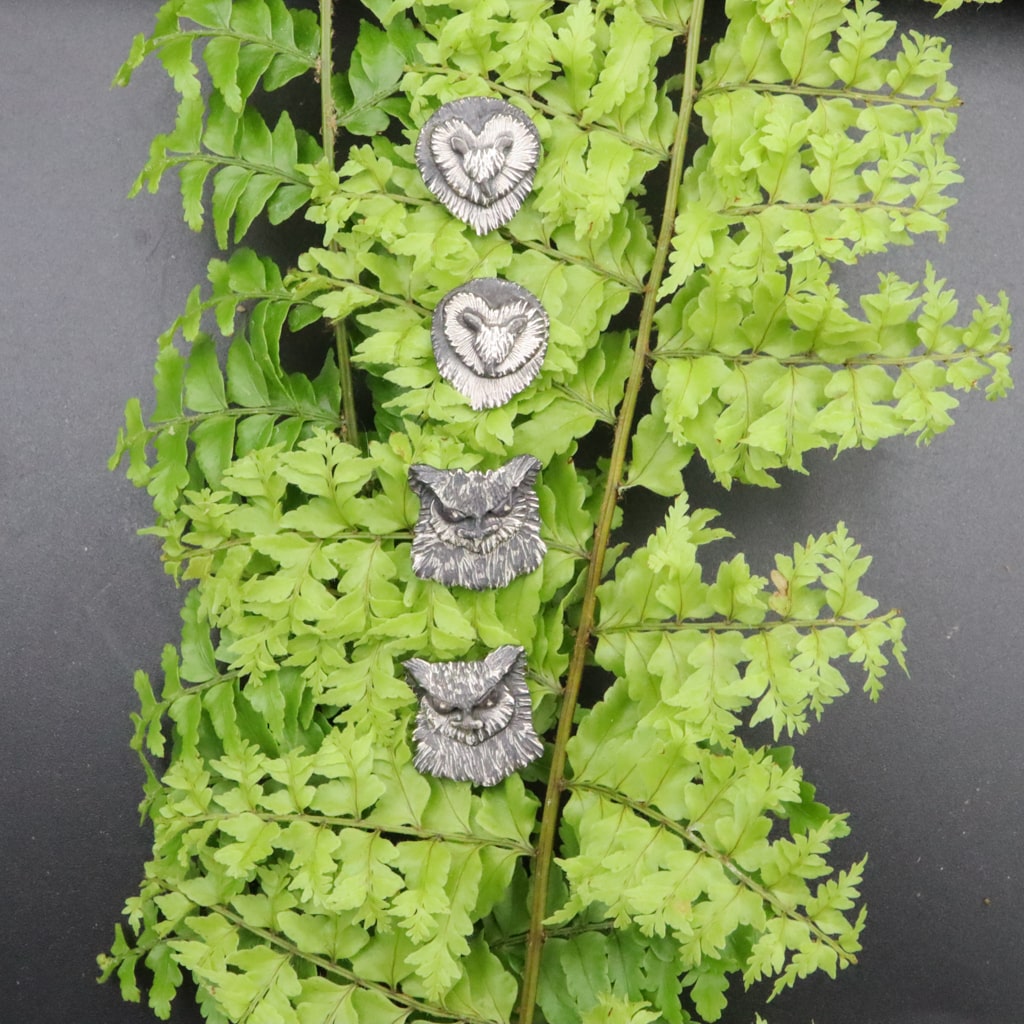 Sterling silver owl faces featuring a pair of barn owls and great horned owls. They are about a half inch tall and shown on a few sprigs of real ferns. 