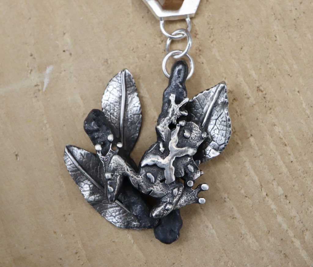 A close up of the hand carved sterling silver spring peeper frog at the bottom of the earrings. He is stretching up on a tree branch and you can see all of his suction cup toes.