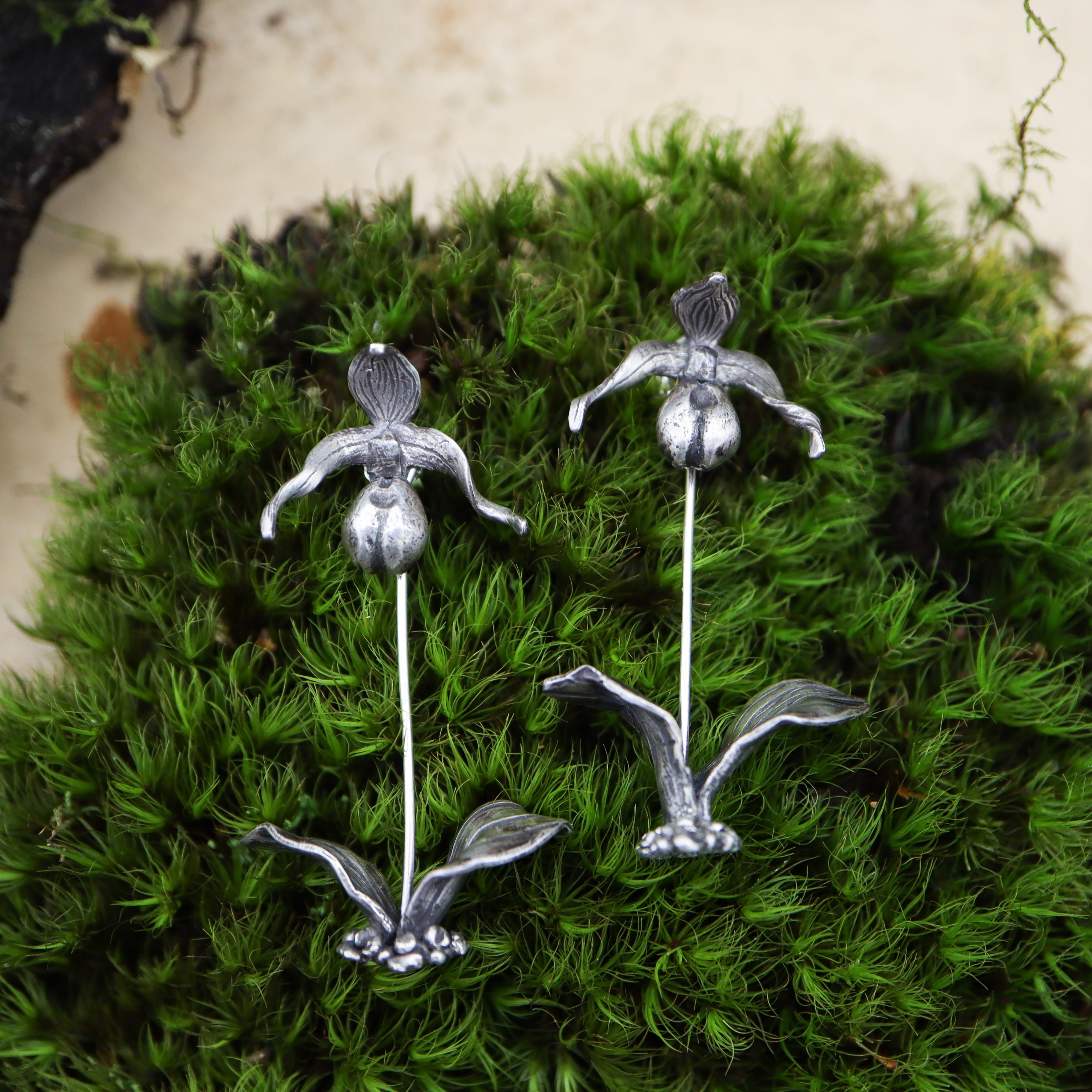 Sterling silver pink lady slipper orchids are shown on a piece of dark green moss.