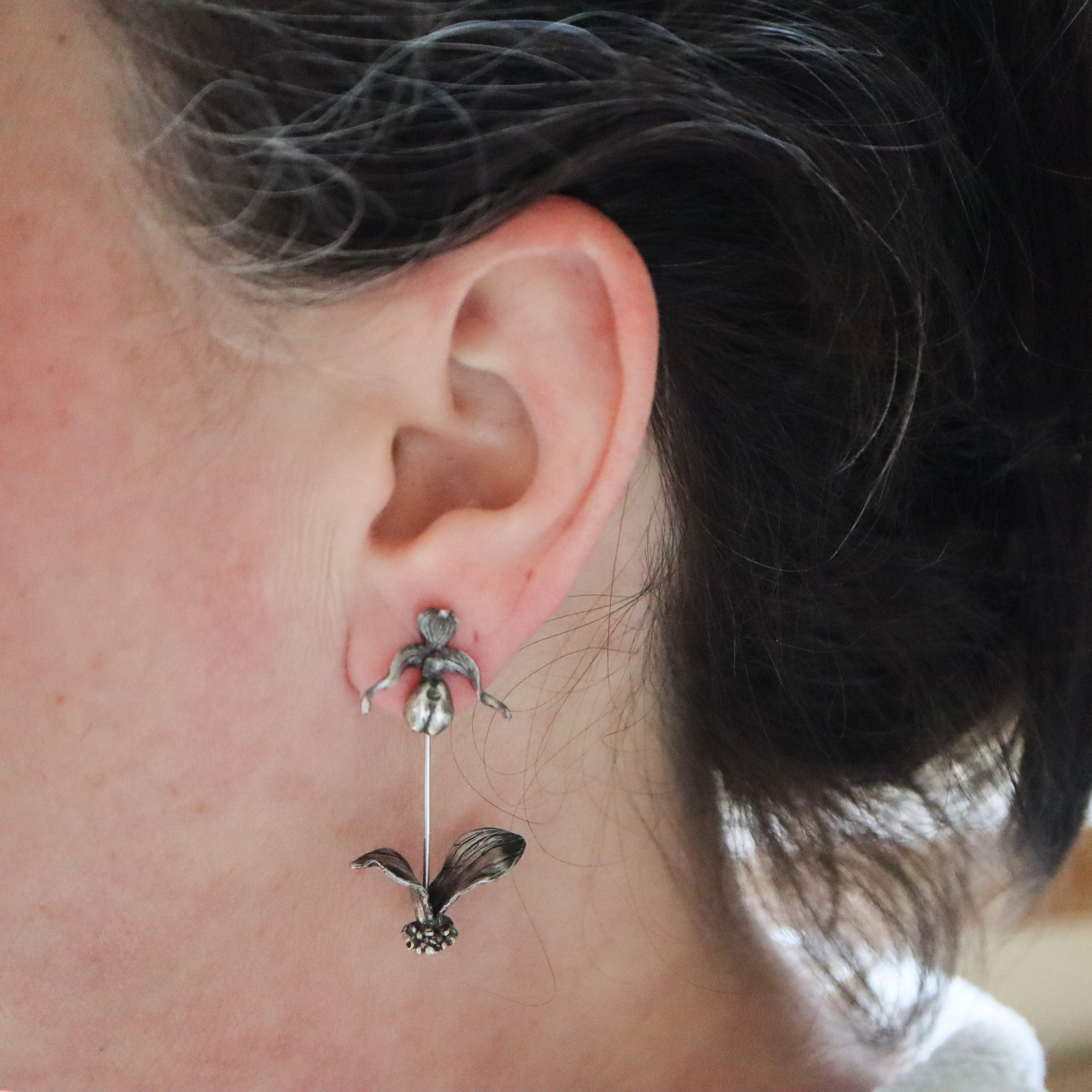 A woman with dark brown hair is shown wearing the pink lady slipper orchid dangle earrings.
