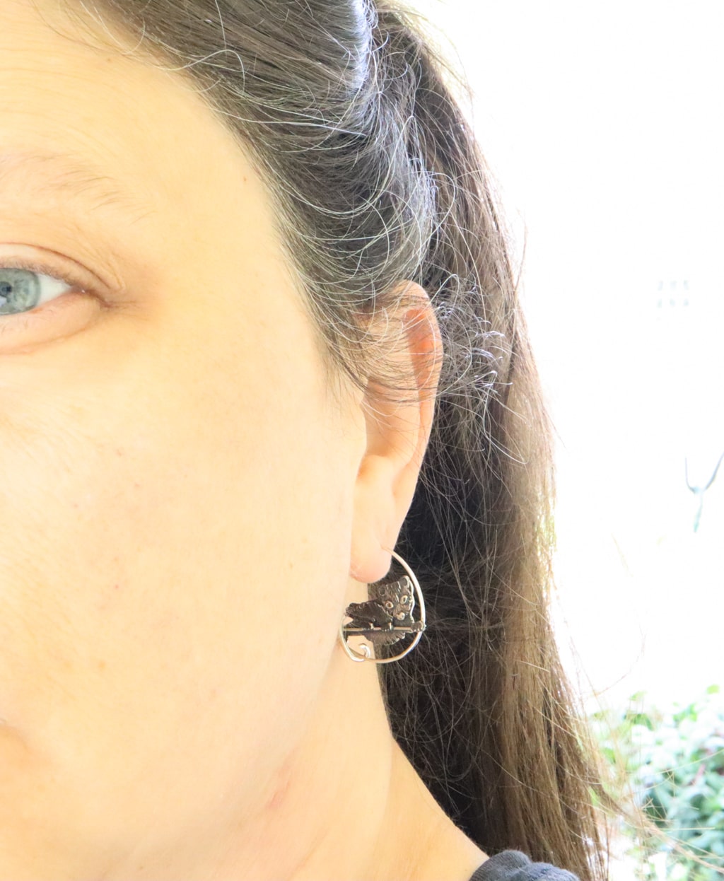 Sterling silver Virginia opossum hoop earrings are being shown worn on a woman with dark brown hair. The earrings are about 1 inch wide and 1 inch tall.