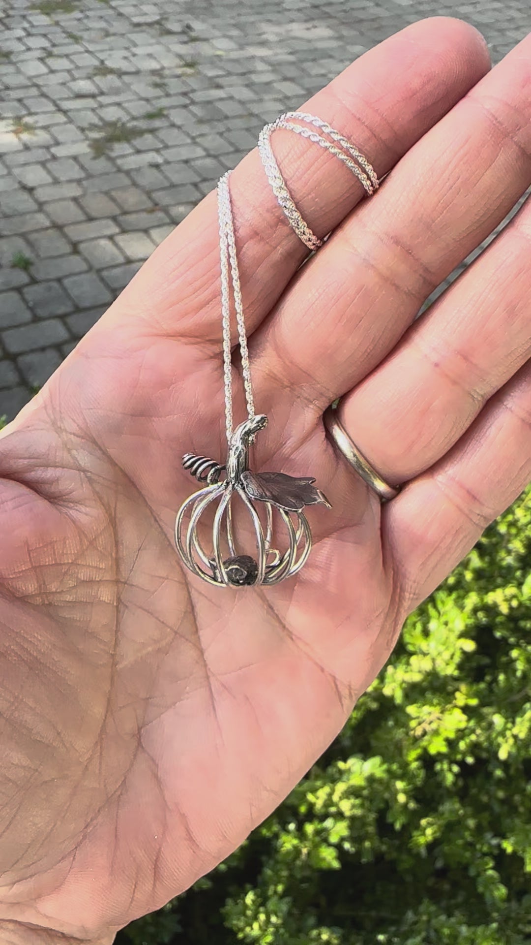 A video of a hand holding a handmade silver pumpkin necklace with a tiny mouse inside of it.