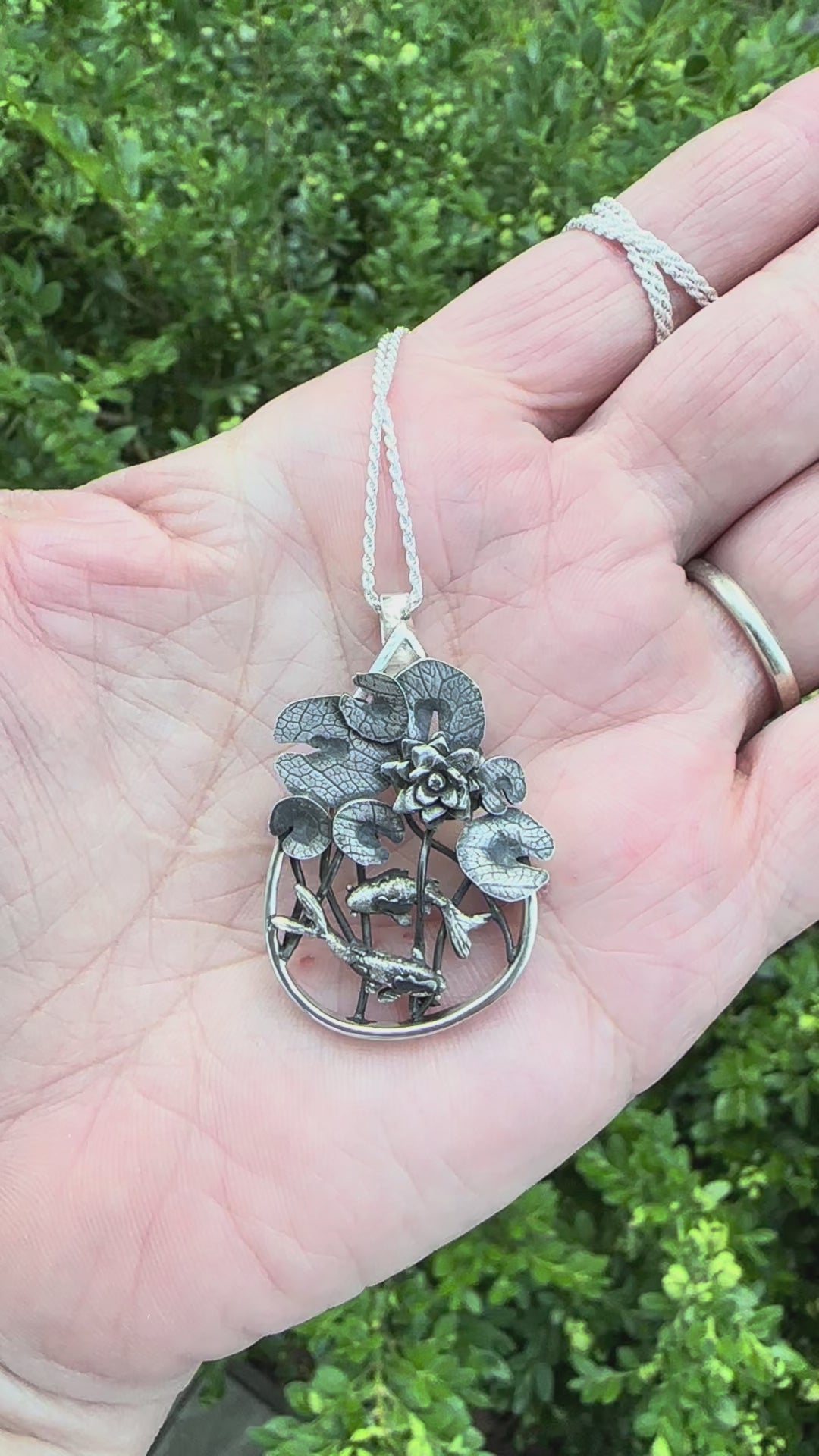 A video showing a hand holding the sterling silver goldfish and lily pad pond necklace.