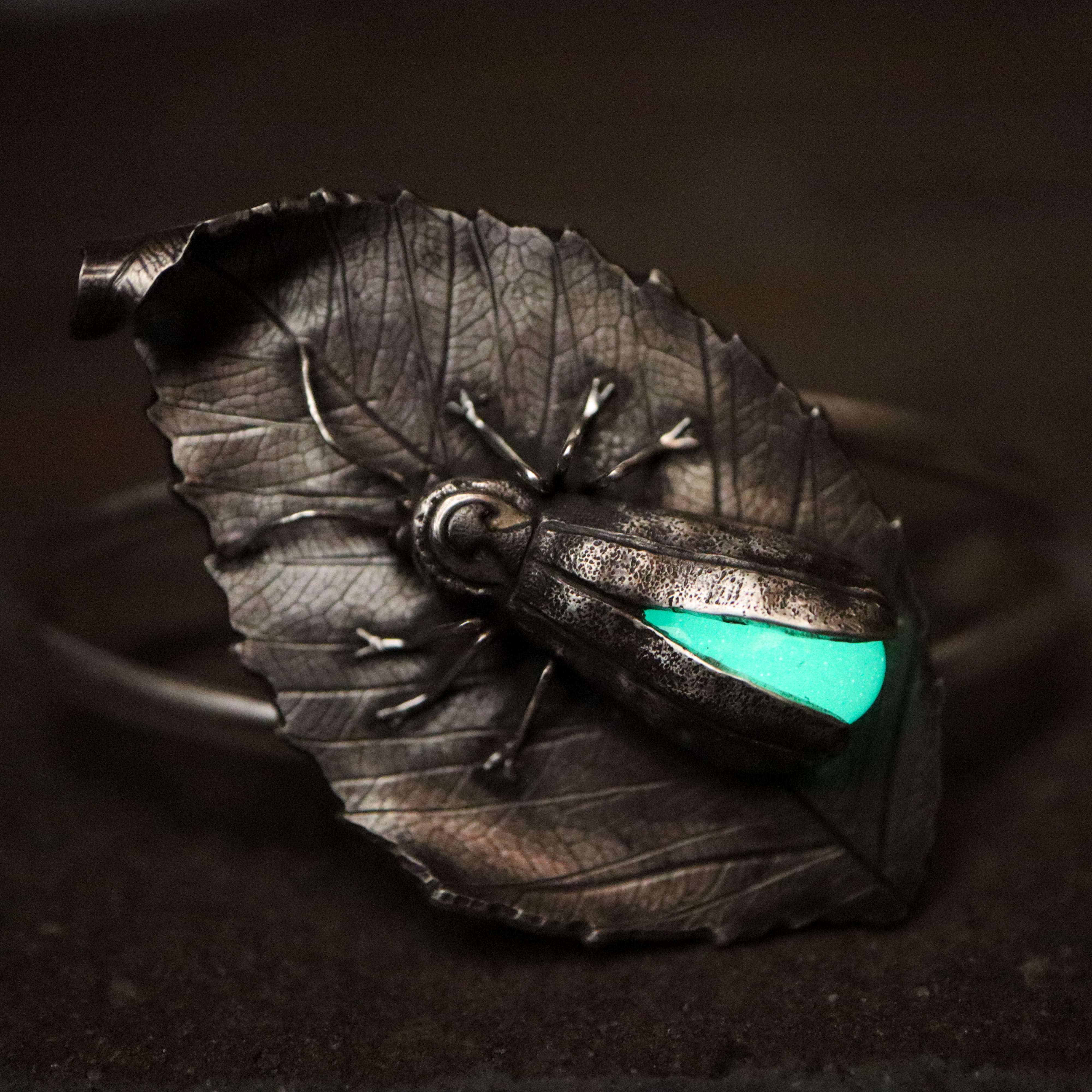 A glow in the dark sterling silver firefly bracelet shown in dim light while the glass abdomen glows.