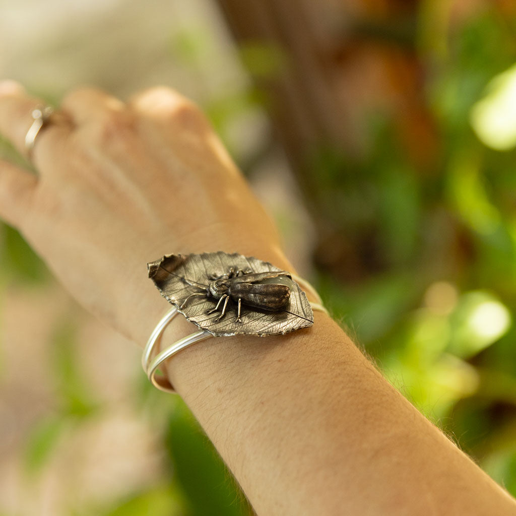 Silver beech leaf-shaped and glow in the dark firefly bracelet on a wrist with a blurred natural background