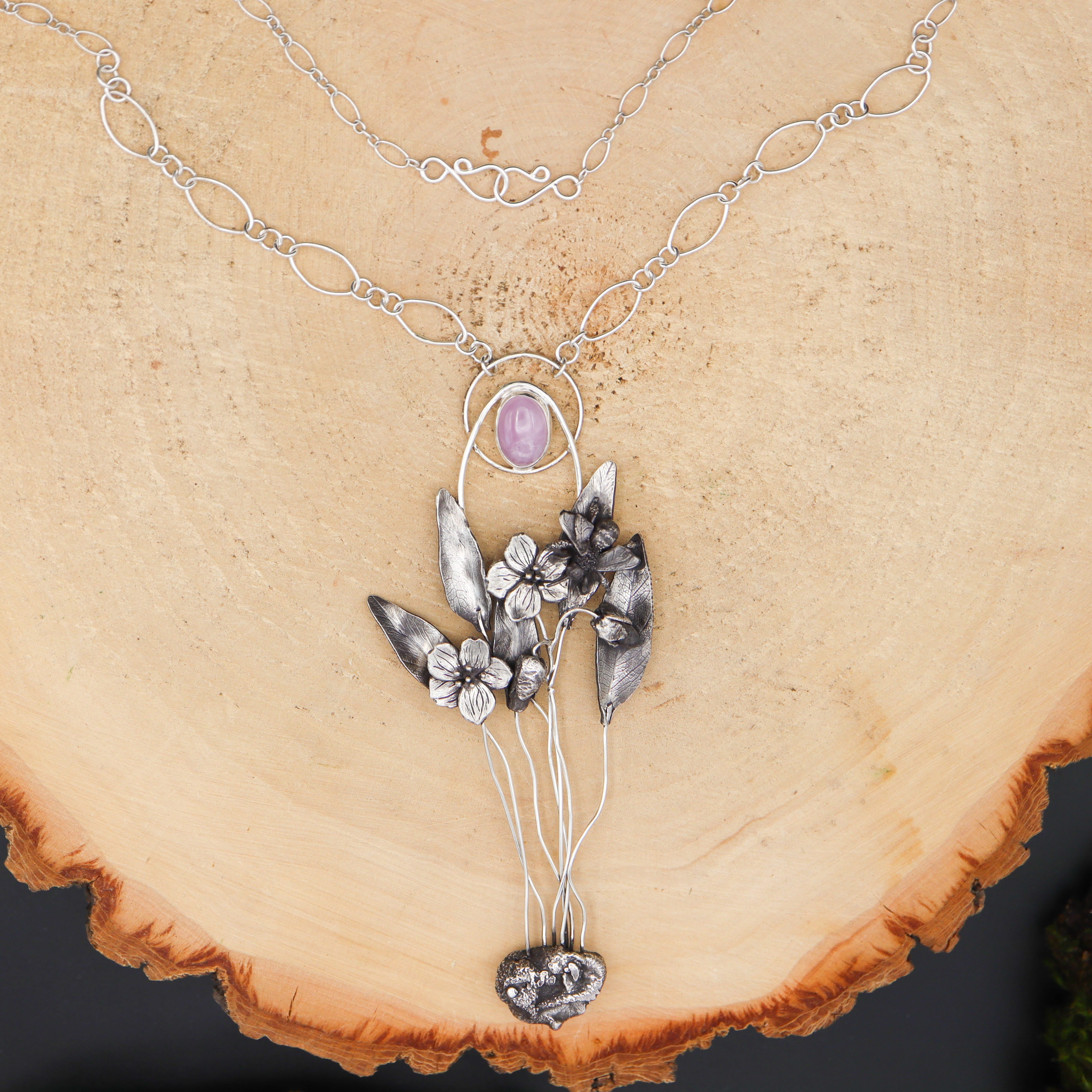 Silver necklace with floral pendant on a wooden surface