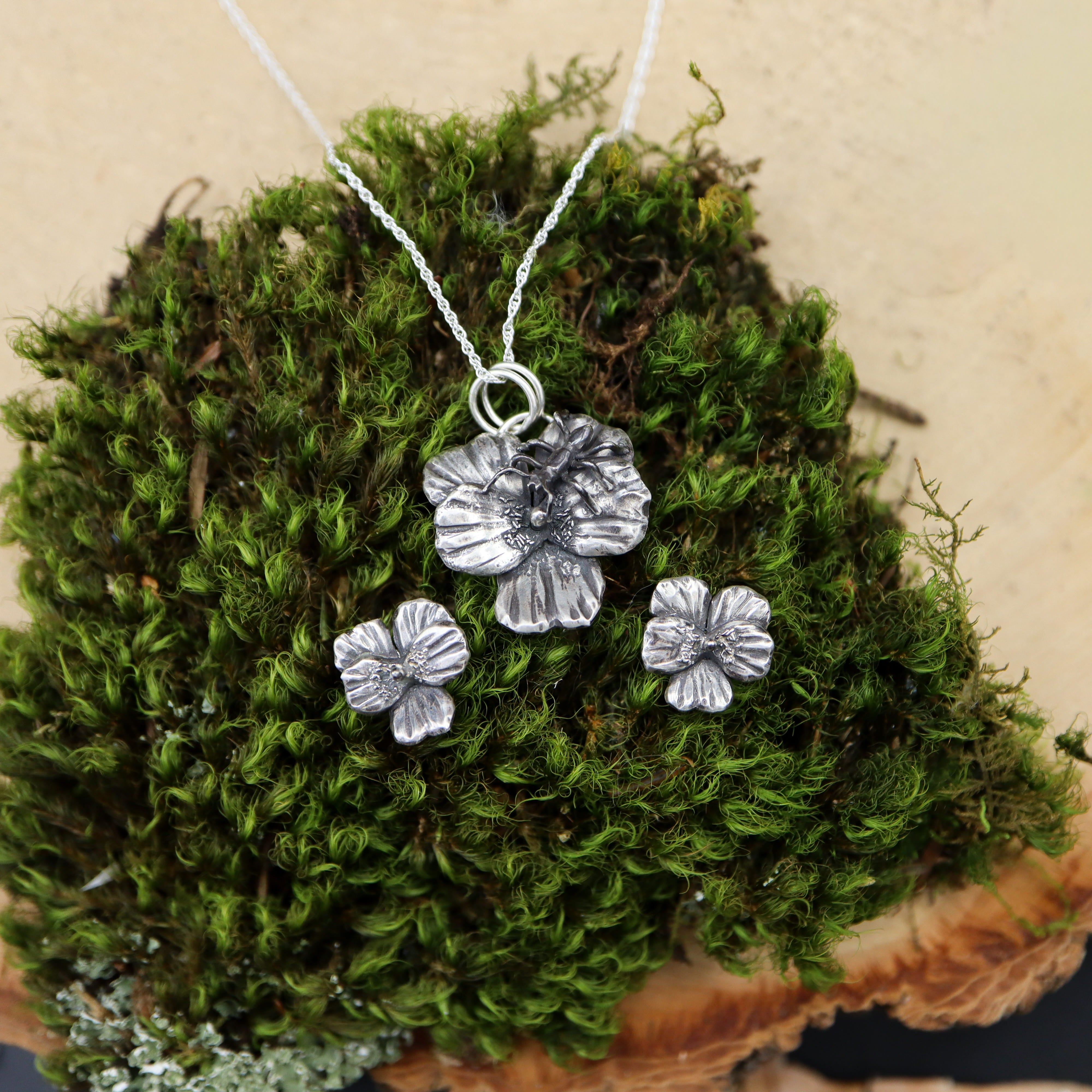 A sterling silver necklace and earring stud set featuring the round-leafed spring ephemeral yellow violet. The necklace has a tiny hand carved ant on it because ants help disperse the seeds of the native wildflower.