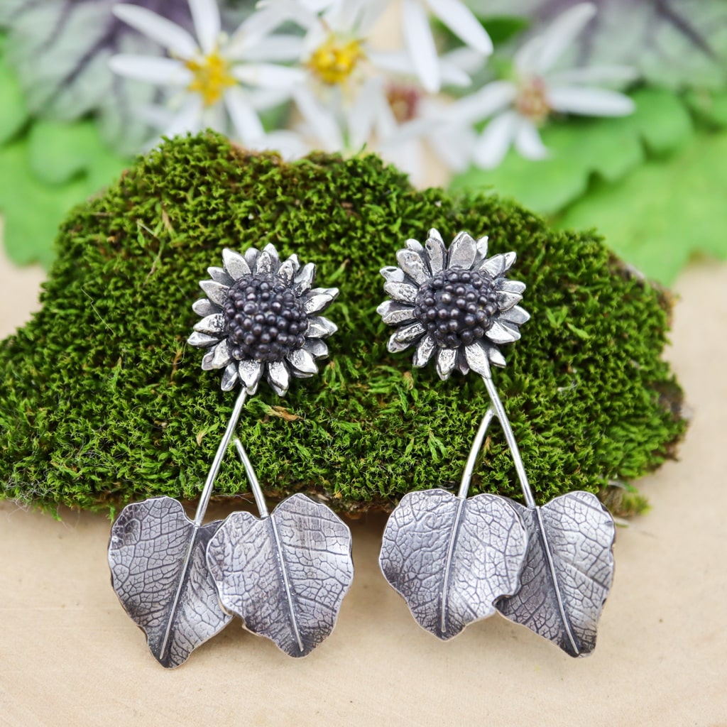 Sterling silver sunflower dangle earrings are shown on a piece of dark green moss.