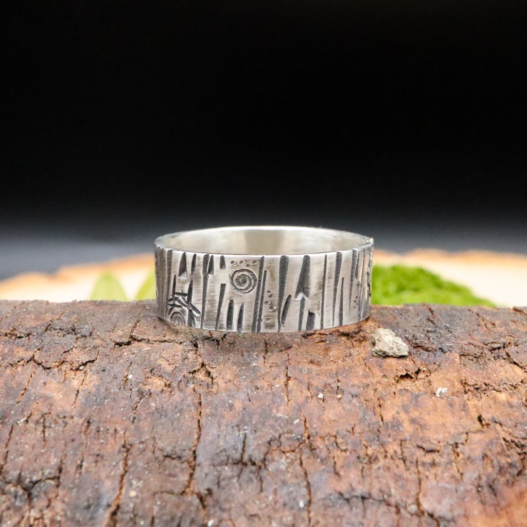 A sterling silver handmade tree bark textured ring is shown on a piece of dark brown wood.