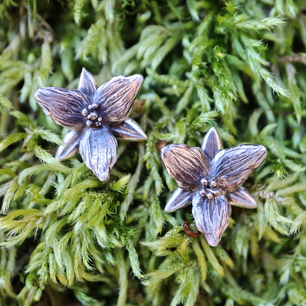 Sterling silver trillium flower earrings shown on some bright green living moss.