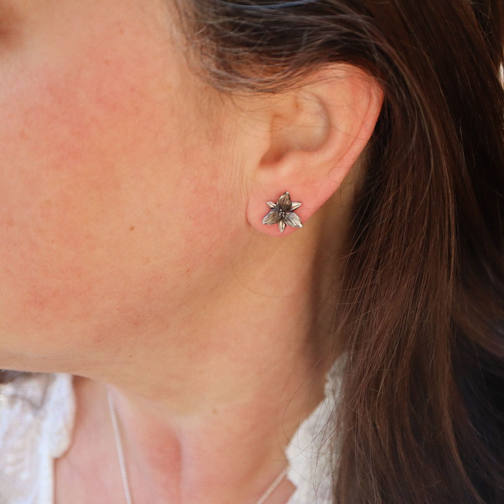 A woman with dark brown hair is shown wearing the sterling silver trillium flower studs.