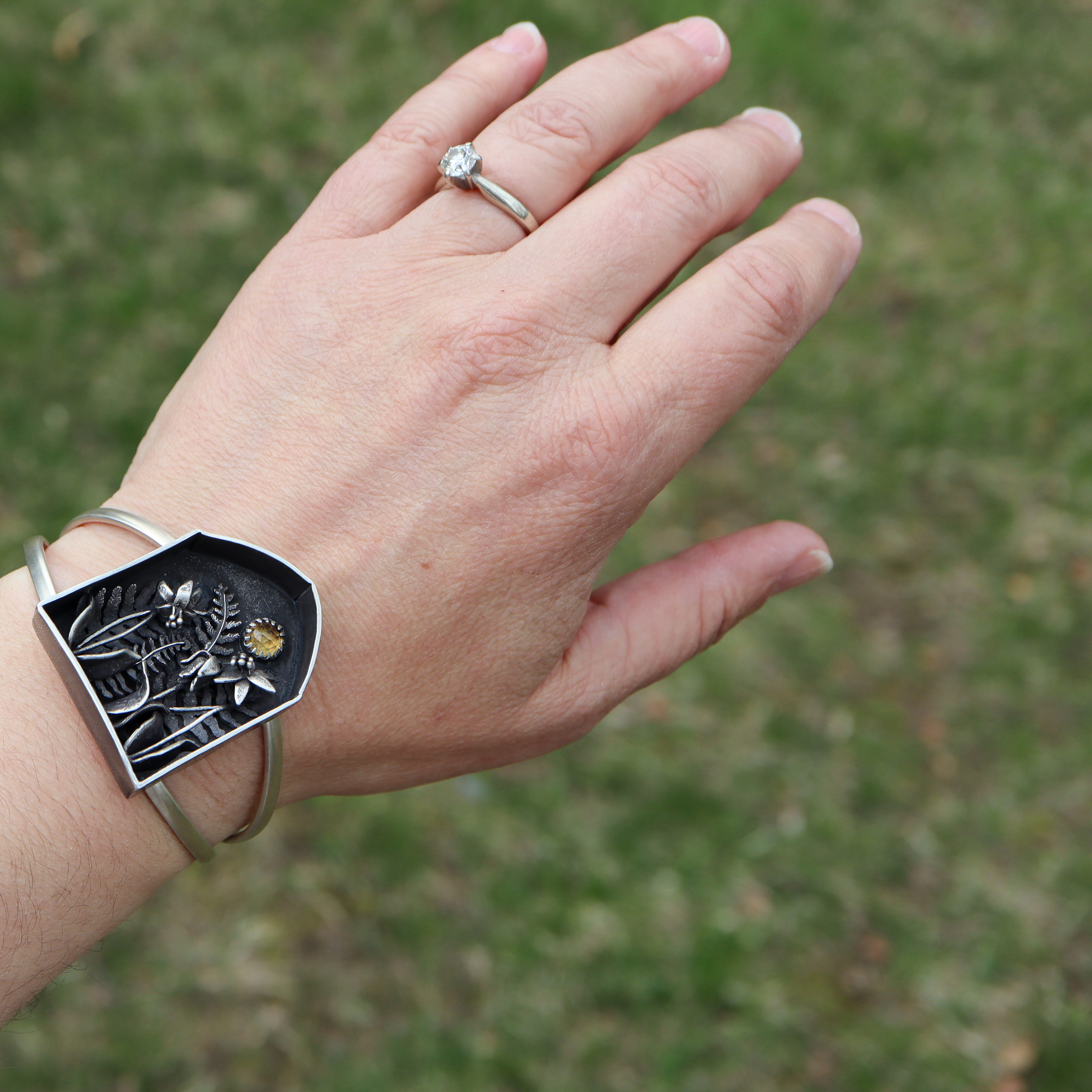 A hand is shown wearing the sterling silver yellow trout lily shadowbox bracelet.