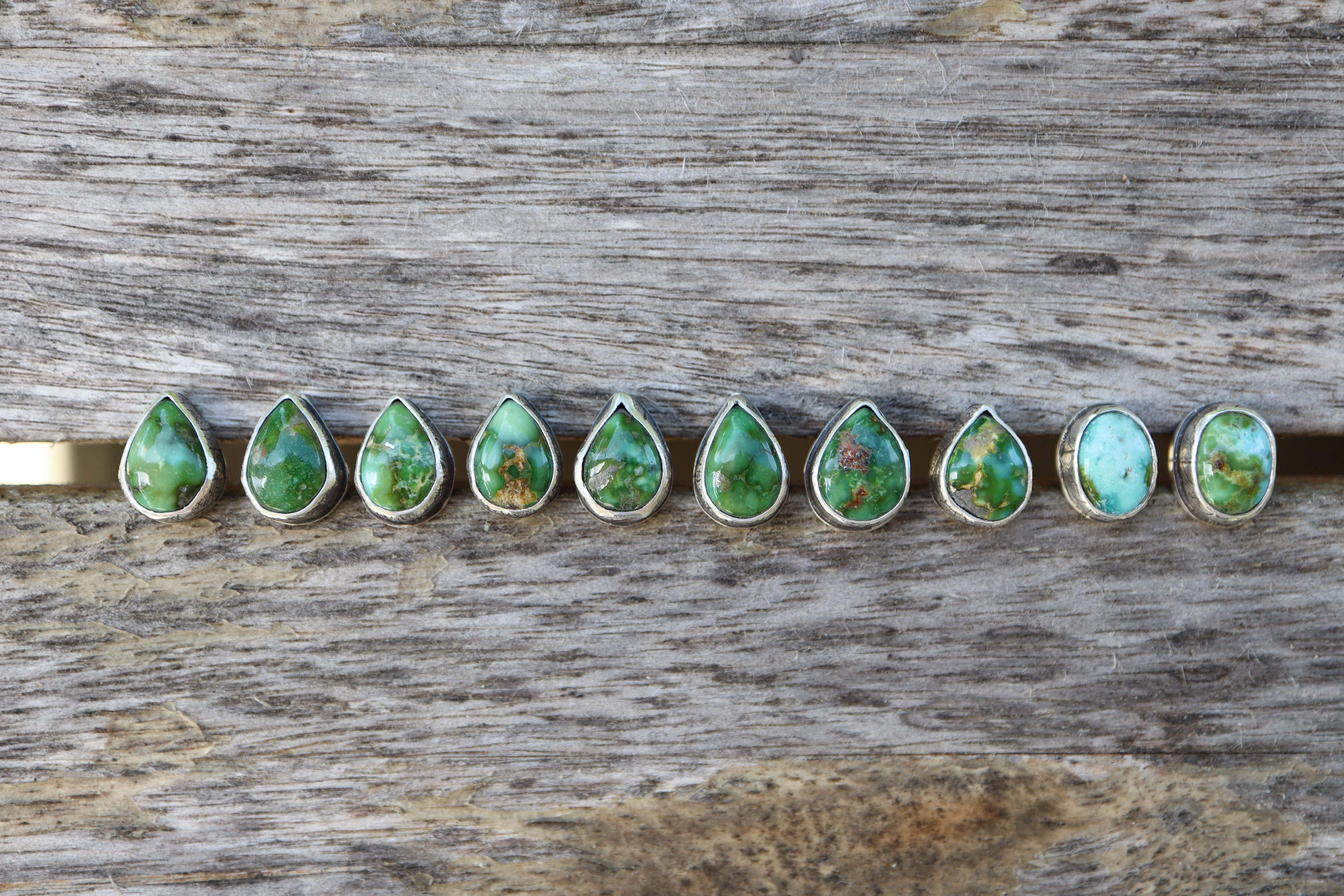 Row of green teardrop-shaped turquoise gemstones on a wooden surface
