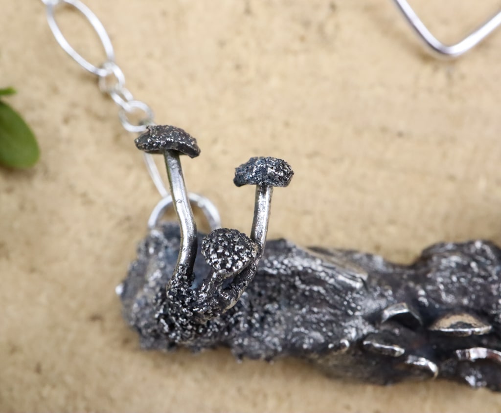 A cluster of tiny sterling silver mushrooms at the end of the silver log.