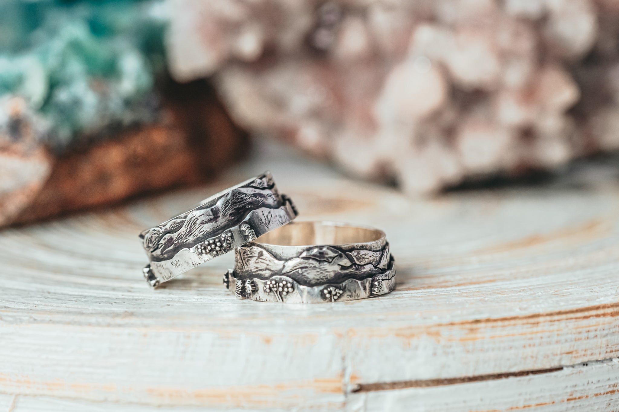 A pair of matching wedding bands depicting the White Mountains in New Hampshire. The rings are shown on a piece of light colored wood.