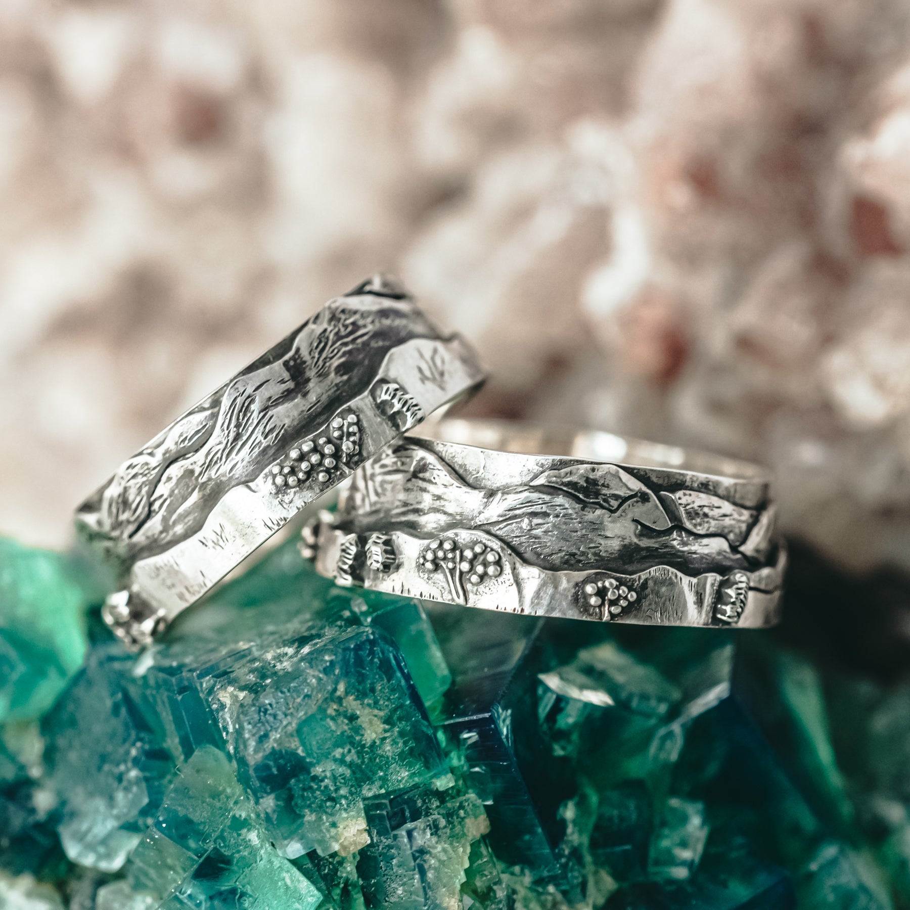 The White Mountains of New Hampshire mountain line on a sterling silver ring. Both rings are shown on a piece of dark green mineral stone.