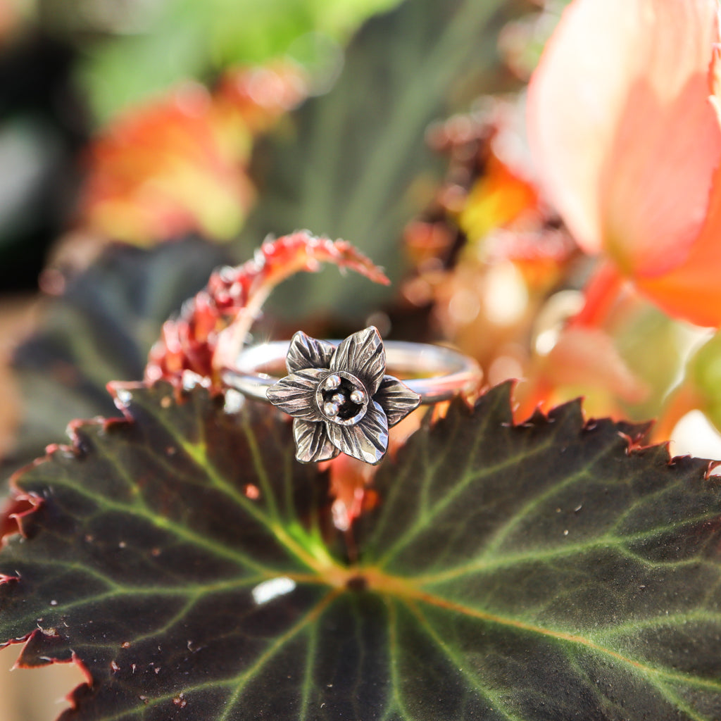 A sterling silver handmade daffodil flower ring is shown on top of a dark green begonia leaf.