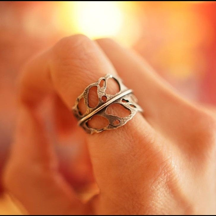 A hand is shown wearing a sterling silver monstera obliqua ring with a soft focus on the background.