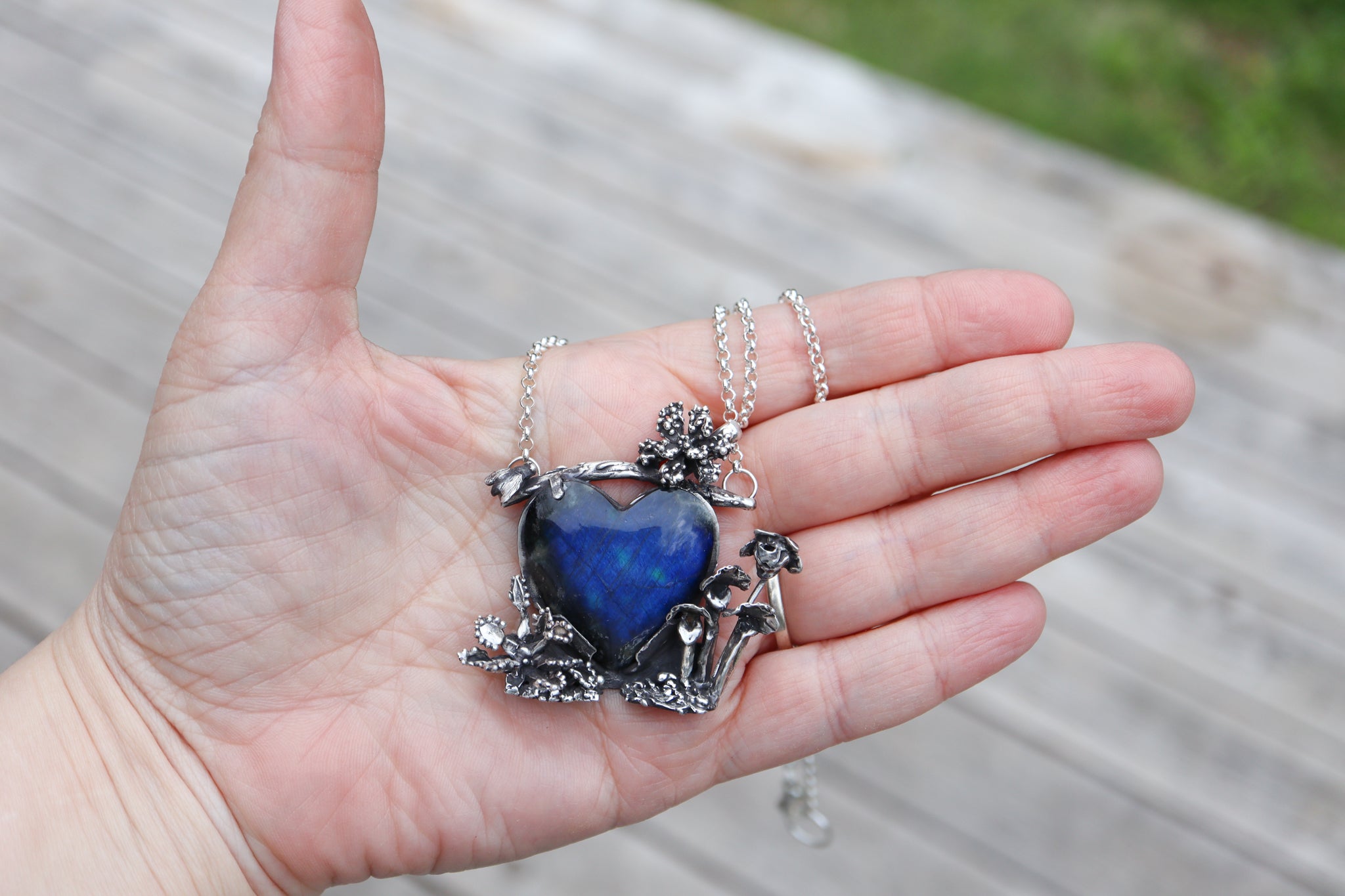 A hand is shown holding the pendant to show it's size. It is about 2 inches tall and a little over 2 inches wide.