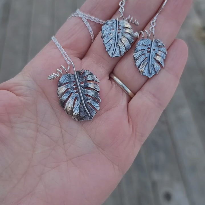 A video showing what a matching set of monstera deliciosa earrings and necklace look like in someone's hand.